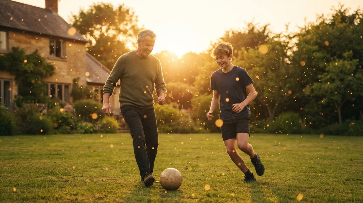 Mann um die 55 spielt an einem Sommerabend mit seinem Sohn auf dem Rasen Fußball