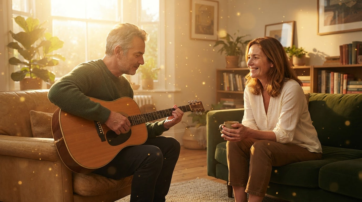 Mann um die 55 übt im Wohnzimmer Gitarrengriffe, eine Frau um die 50 hört ihm lächelnd zu